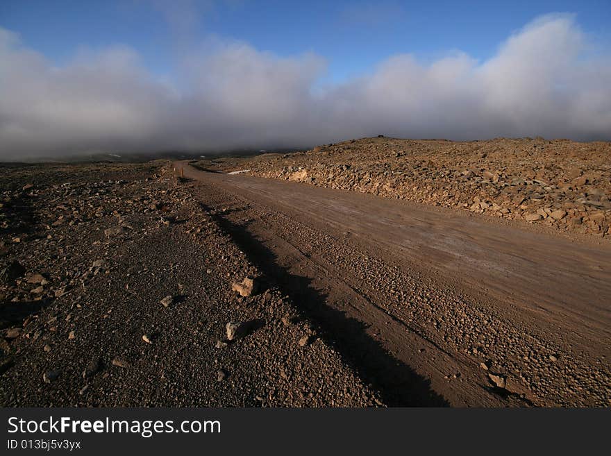 A dirt road running through a stone desert lit by the setting sun. A dirt road running through a stone desert lit by the setting sun.