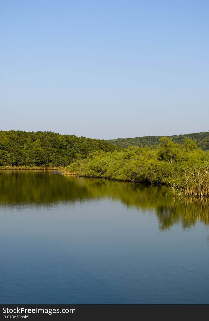 Wide river and shores with trees and green on a deep blue sky