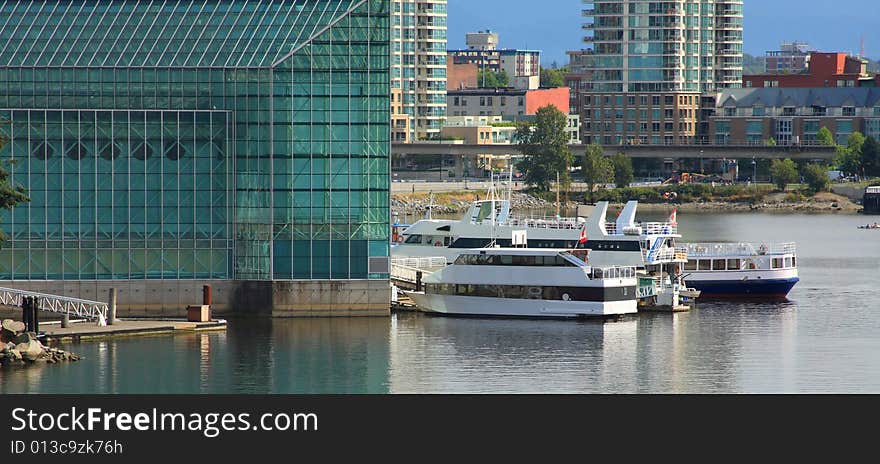 Several boats docked at a glass building, with the city in the background. Several boats docked at a glass building, with the city in the background.