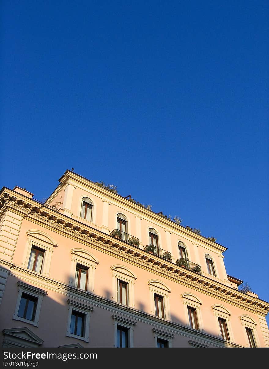 Facade of upper levels of a pretty apartment building in Rome, sunlit against a blue sky. Facade of upper levels of a pretty apartment building in Rome, sunlit against a blue sky