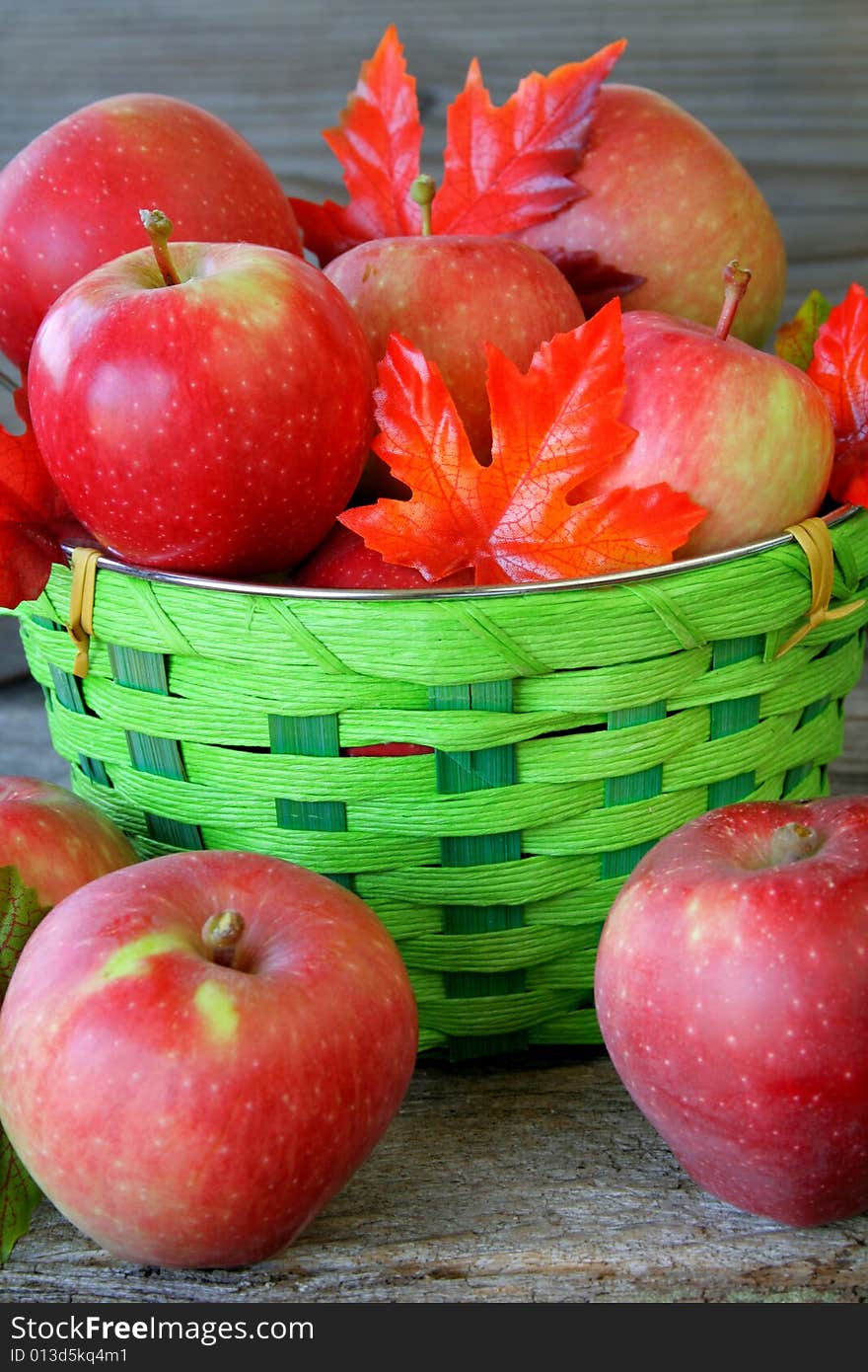 A close up of a basket full of apples with silk fall leaves. A close up of a basket full of apples with silk fall leaves.