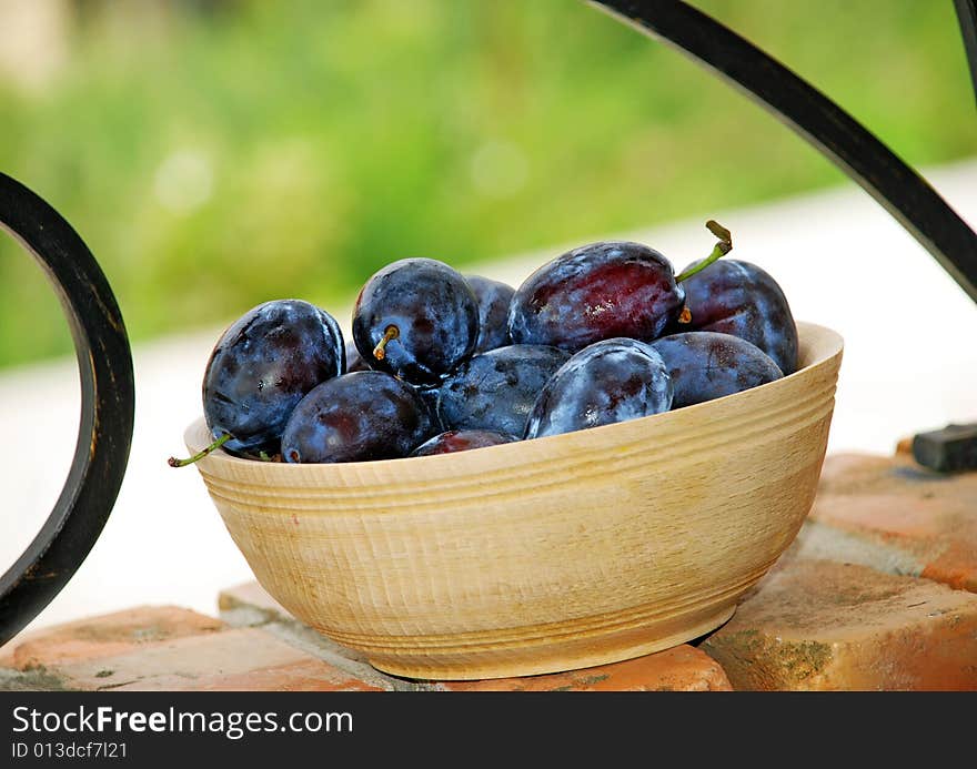 Blue ripe plums in wooden bowl over brick fence. Blue ripe plums in wooden bowl over brick fence