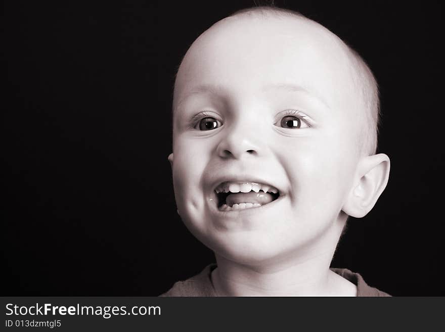 Blonde toddler against a black background with a big smile