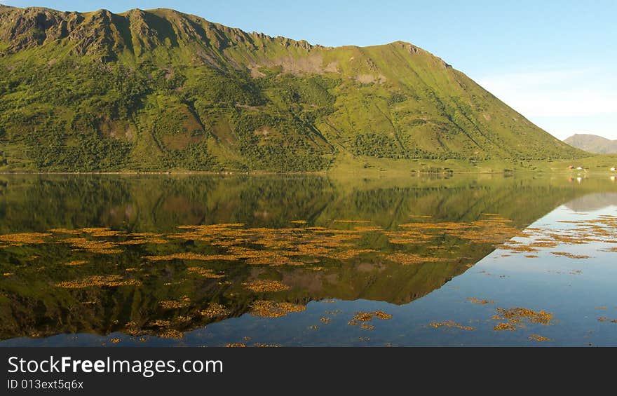 Cape reflecting in a fjord with the midnight's sun, Lofoten islands, Arctic ocean. Cape reflecting in a fjord with the midnight's sun, Lofoten islands, Arctic ocean