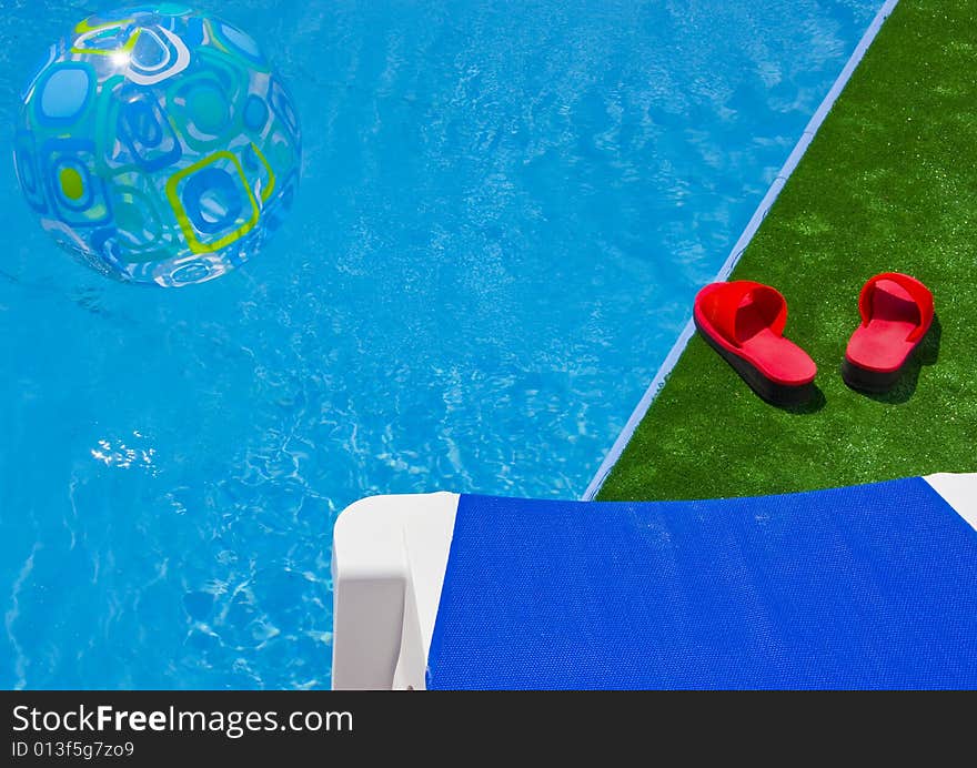 Swimming pool with sun lounger detail, red sandals and water ball. Swimming pool with sun lounger detail, red sandals and water ball