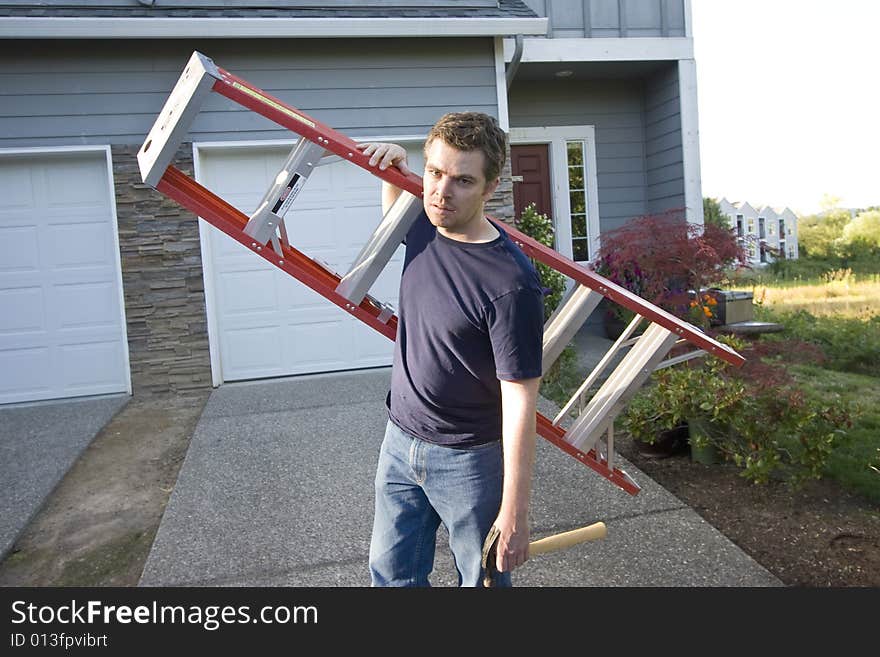 Angry, frowning man standing in front of house holding ladder and hammer. Horizontally framed photo. Angry, frowning man standing in front of house holding ladder and hammer. Horizontally framed photo.