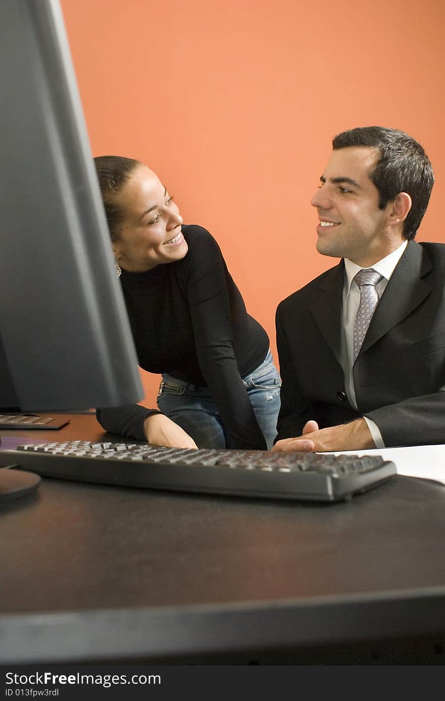 Businessman and woman looking at each other and smiling. They are in front of a computer. Vertically framed photo. Businessman and woman looking at each other and smiling. They are in front of a computer. Vertically framed photo.