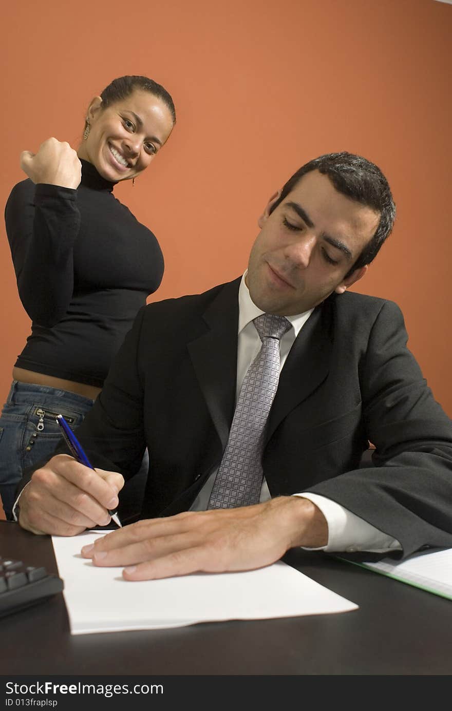 Businessman working at his desk while his co-worker pretends to be angry with him. Vertically framed photo. Businessman working at his desk while his co-worker pretends to be angry with him. Vertically framed photo