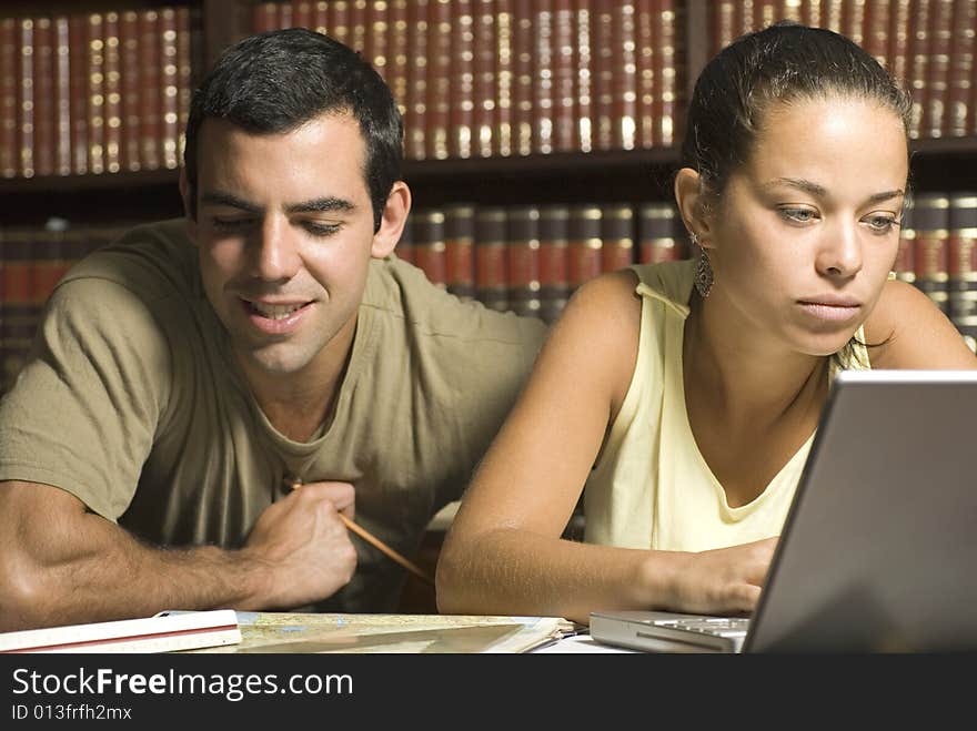 Young couple study together in an office with many books and a computer. Horizontally framed photo. Young couple study together in an office with many books and a computer. Horizontally framed photo.