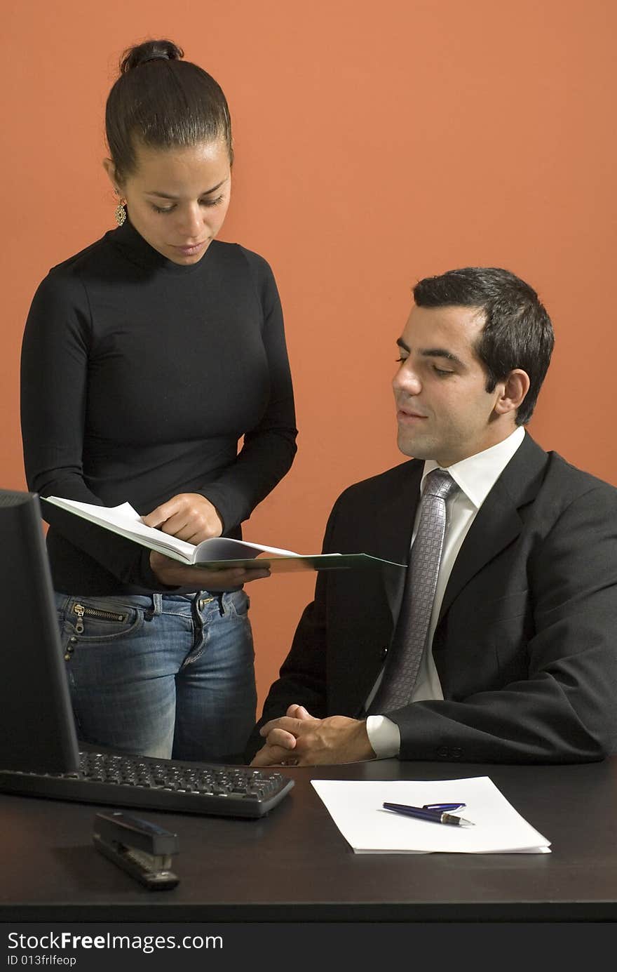 Businessman seated at desk while his co-worker shows him paperwork. Vertically framed photo. Businessman seated at desk while his co-worker shows him paperwork. Vertically framed photo.