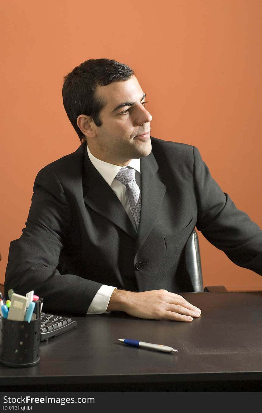 Businessman seated at desk looking off into the distance. Vertically framed photo. Businessman seated at desk looking off into the distance. Vertically framed photo.