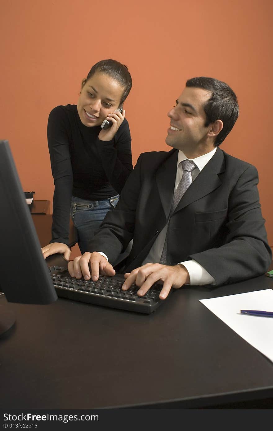 Businessman at his computer looks at his employee as she talks on a cell phone. Vertically framed photo. Businessman at his computer looks at his employee as she talks on a cell phone. Vertically framed photo.