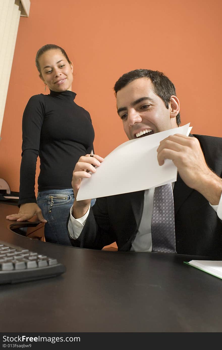 Businessman jokes around by putting a paper in his mouth as his co-worker watches. Vertically framed photo. Businessman jokes around by putting a paper in his mouth as his co-worker watches. Vertically framed photo