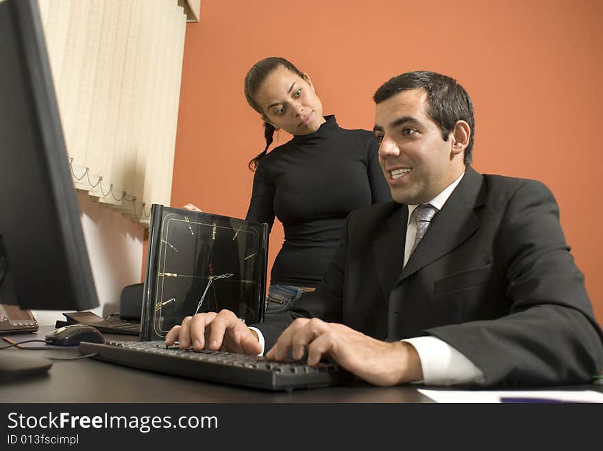 Businessman sits at his desk and looks at his computer while his co-worker stands up looking at him. Vertically framed photo. Businessman sits at his desk and looks at his computer while his co-worker stands up looking at him. Vertically framed photo.