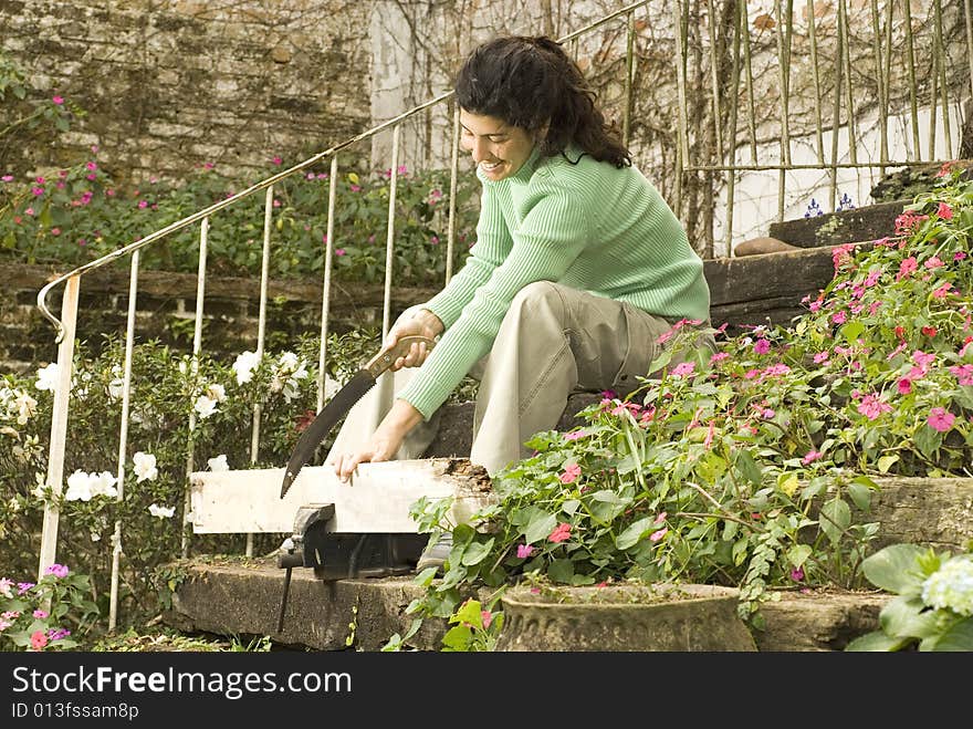 Woman sitting on stairs holds a board in a vice. She is smiling and sawing the board. Horizontally framed photo. Woman sitting on stairs holds a board in a vice. She is smiling and sawing the board. Horizontally framed photo.