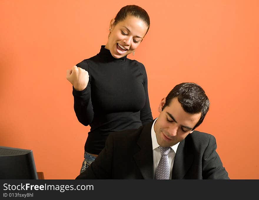 Businessman sits at his desk as his co-worker stands behind him and jokes around. Horizontally framed photo. Businessman sits at his desk as his co-worker stands behind him and jokes around. Horizontally framed photo.