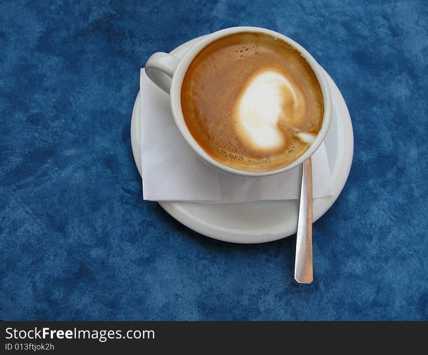 A delicious fresh hot Italian cappuccino in white cup shown fromt top on blue background