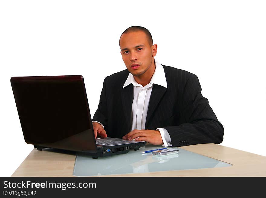 A young businessman sitting by desk at office working on the laptop with cellphone on the table. Isolated over white. A young businessman sitting by desk at office working on the laptop with cellphone on the table. Isolated over white.