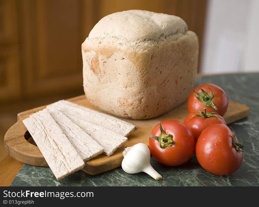 Bread in a breadbord with tomato and garlic on a green table. Bread in a breadbord with tomato and garlic on a green table