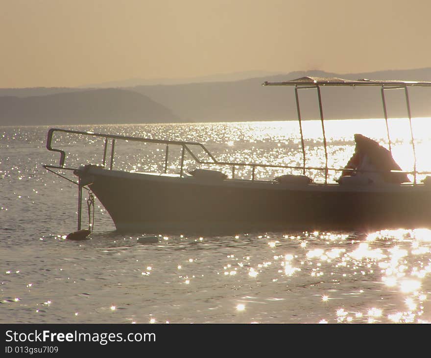 Boat silhouette in the sunset, sunrays glitter on the water, island in the background. Boat silhouette in the sunset, sunrays glitter on the water, island in the background