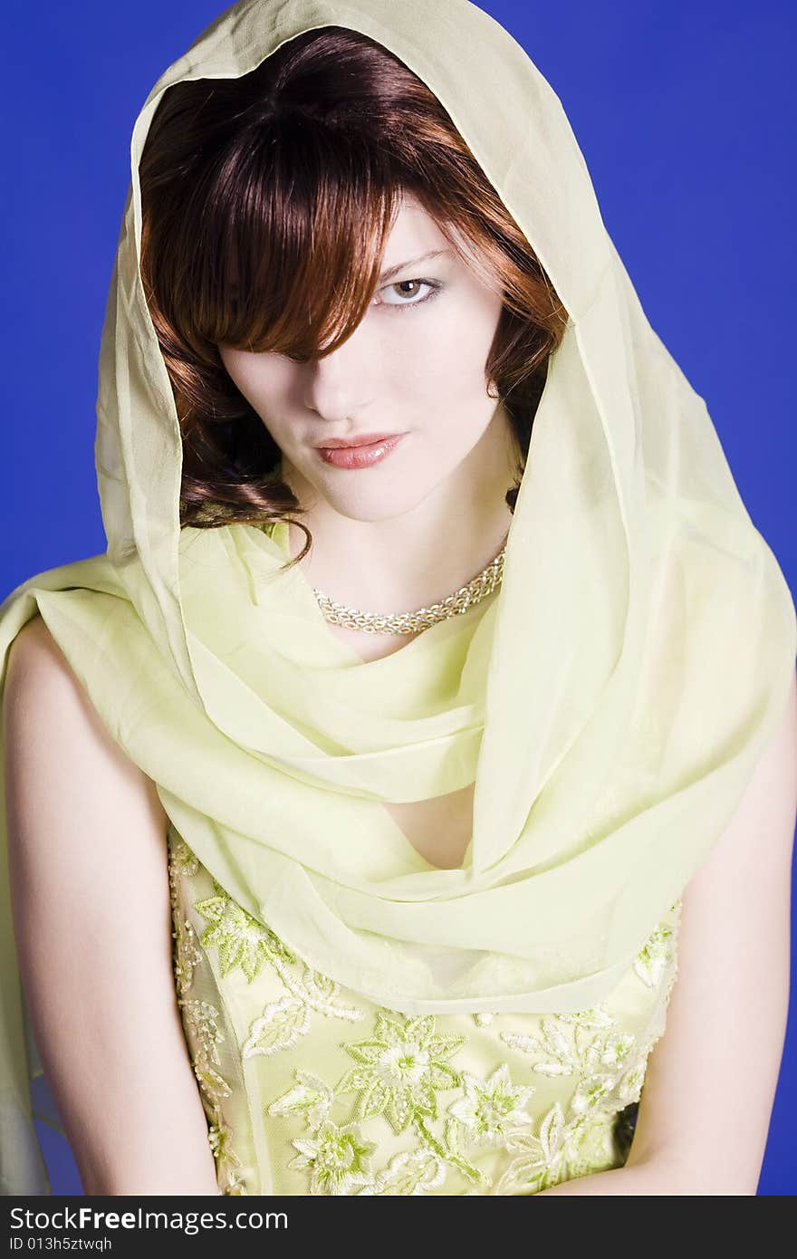 Beautiful young woman wearing green dress with a scarf around her head against a blue back ground. Beautiful young woman wearing green dress with a scarf around her head against a blue back ground