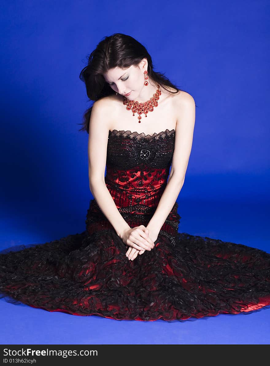 Beautiful young woman wearing red sleeve less evening gown, posing in front of a blue back ground. Beautiful young woman wearing red sleeve less evening gown, posing in front of a blue back ground