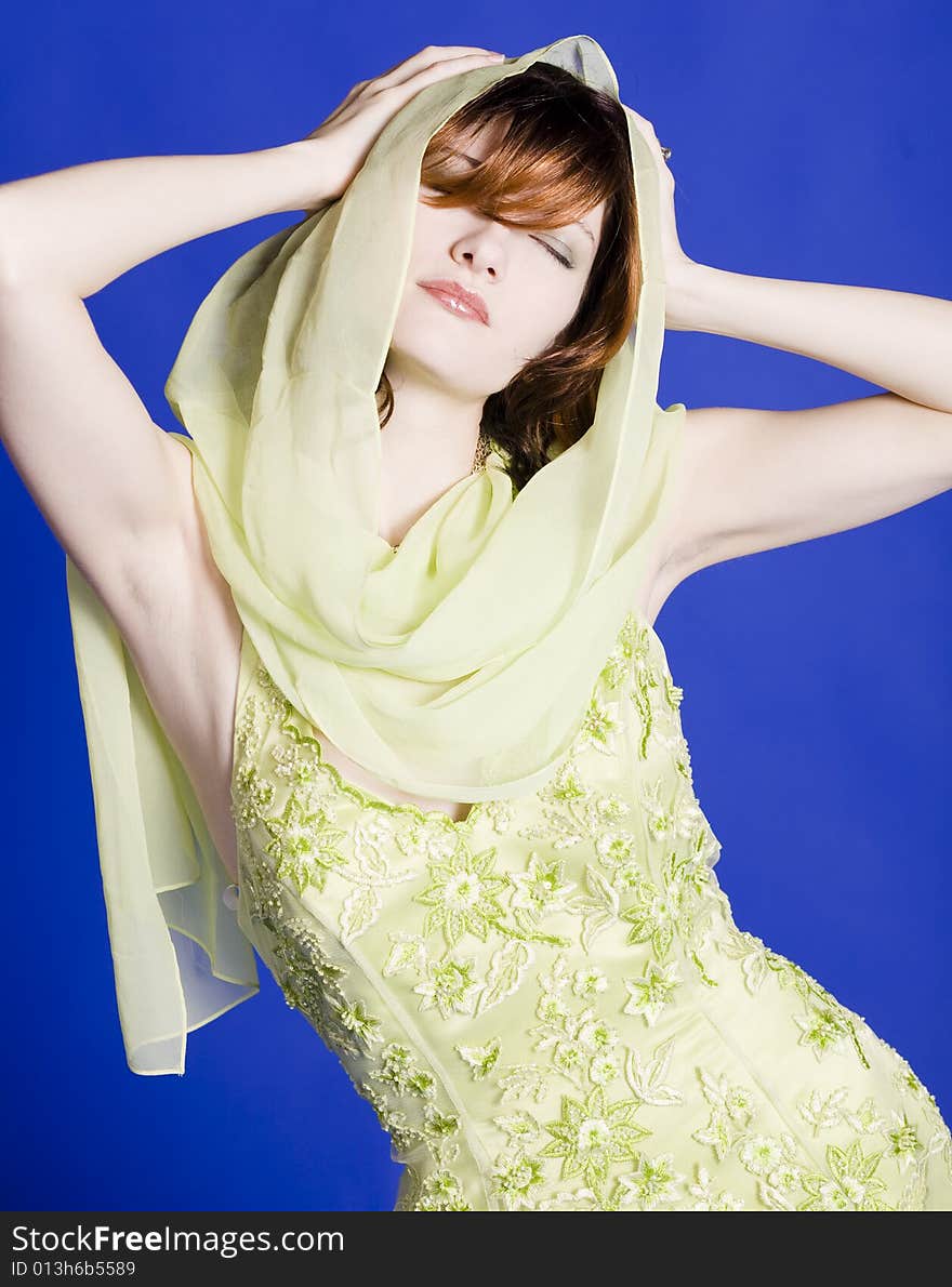 Beautiful young woman wearing green dress with a scarf around her head against a blue back ground. Beautiful young woman wearing green dress with a scarf around her head against a blue back ground