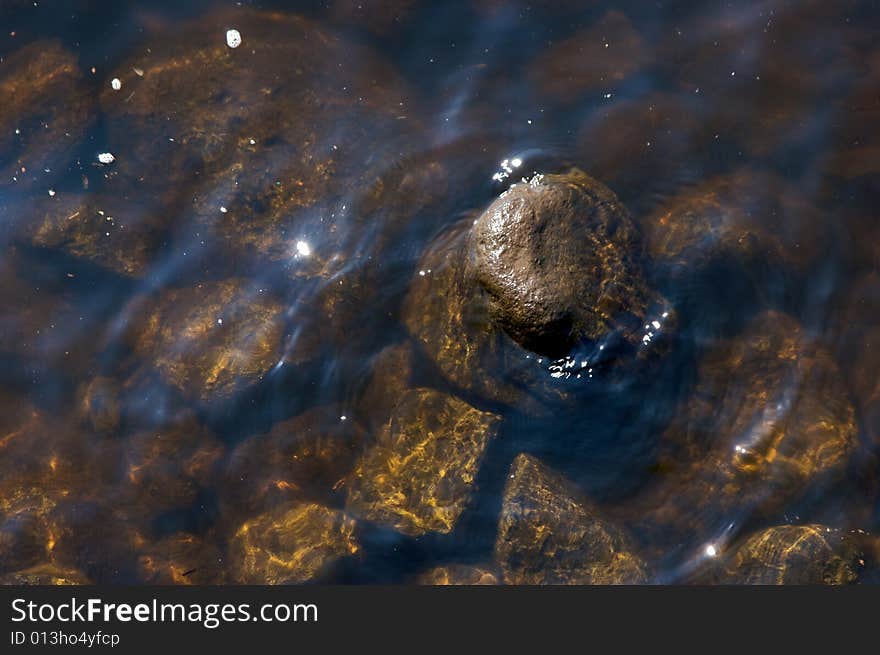 Wet rock sticking out above the surface of the water surrounded by other stones