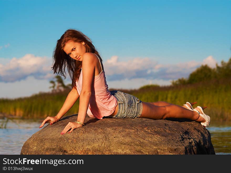 Teenage girl laying on a stone in light of the evening sun