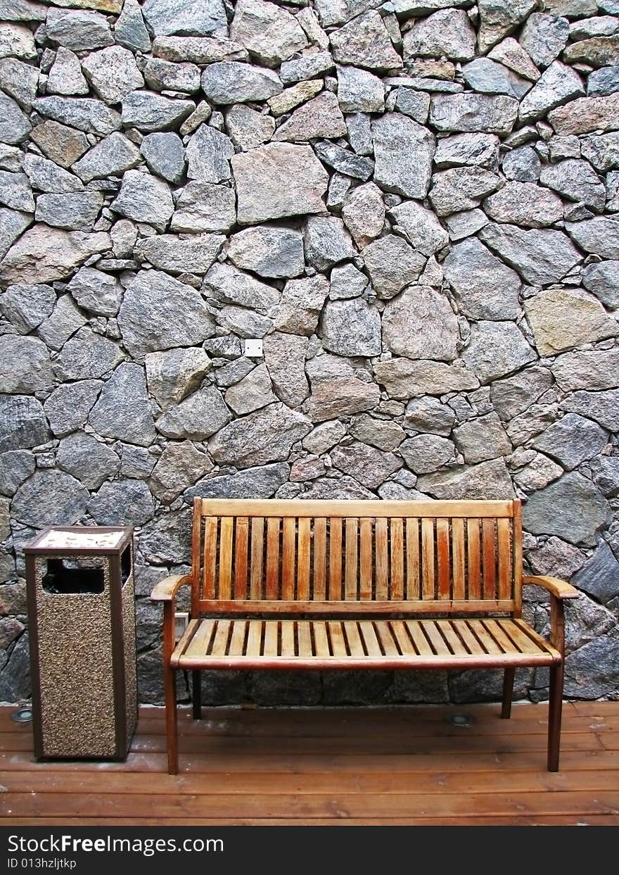 A wood armchair and a ashtray against a stone wall.