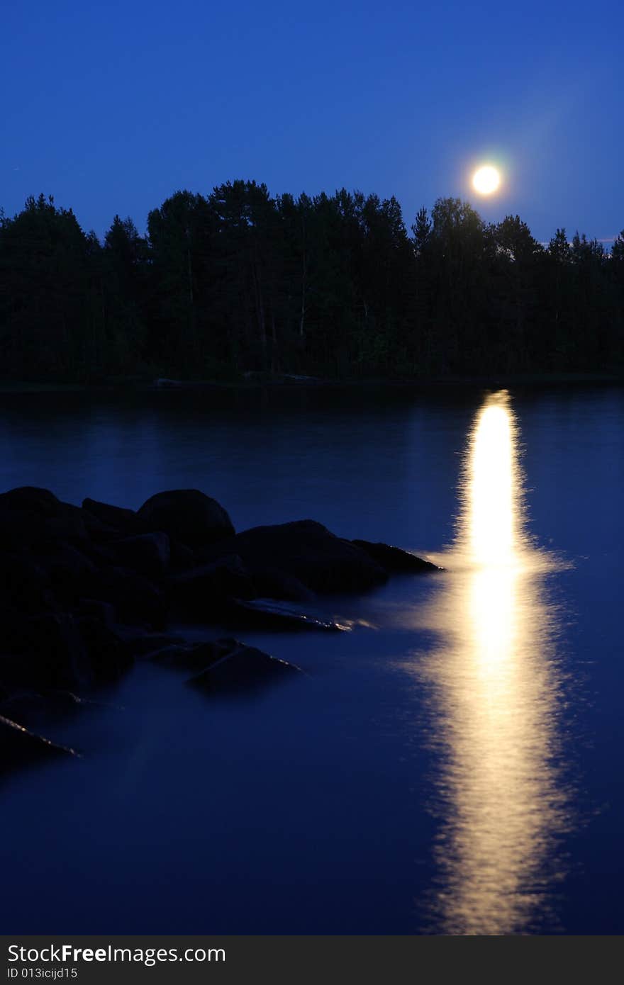 Moon rising and reflecting in the still water of a lake