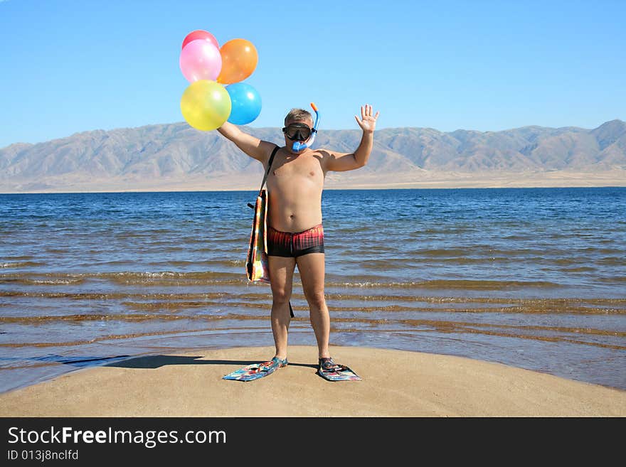 Man with mask, flippers and balloons is salutation  on the beach