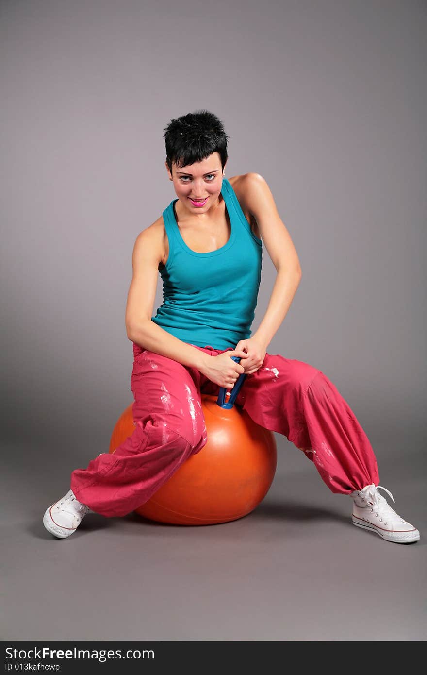 Young woman in sportswear sits on orange ball