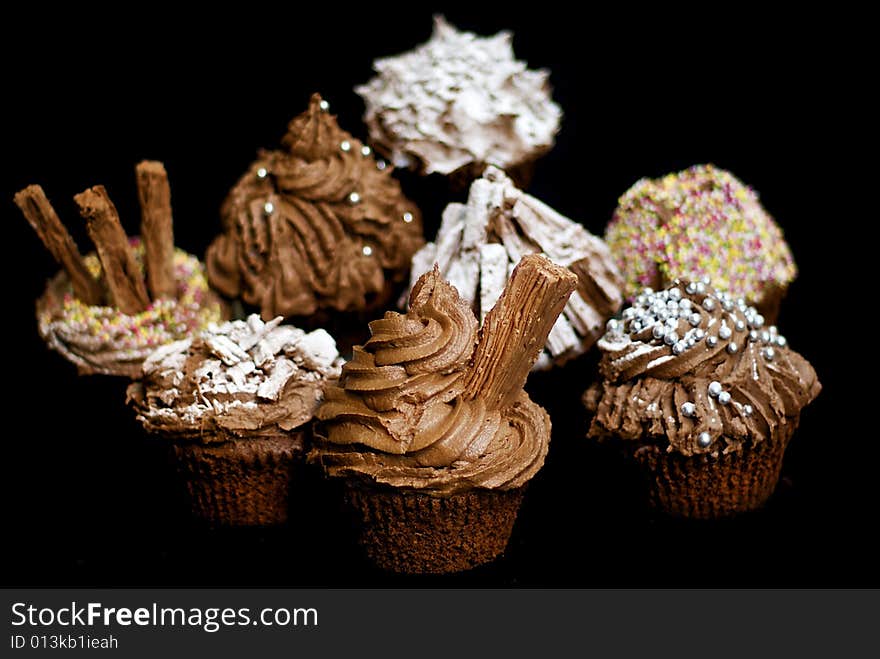 Cup cakes/Muffins suitable for a birthday card or celebration card.chocolate fondant icing and silver balls, icing sugar, flakes and sprinkles, shallow depth of field to isolate foremost cake. Cup cakes/Muffins suitable for a birthday card or celebration card.chocolate fondant icing and silver balls, icing sugar, flakes and sprinkles, shallow depth of field to isolate foremost cake