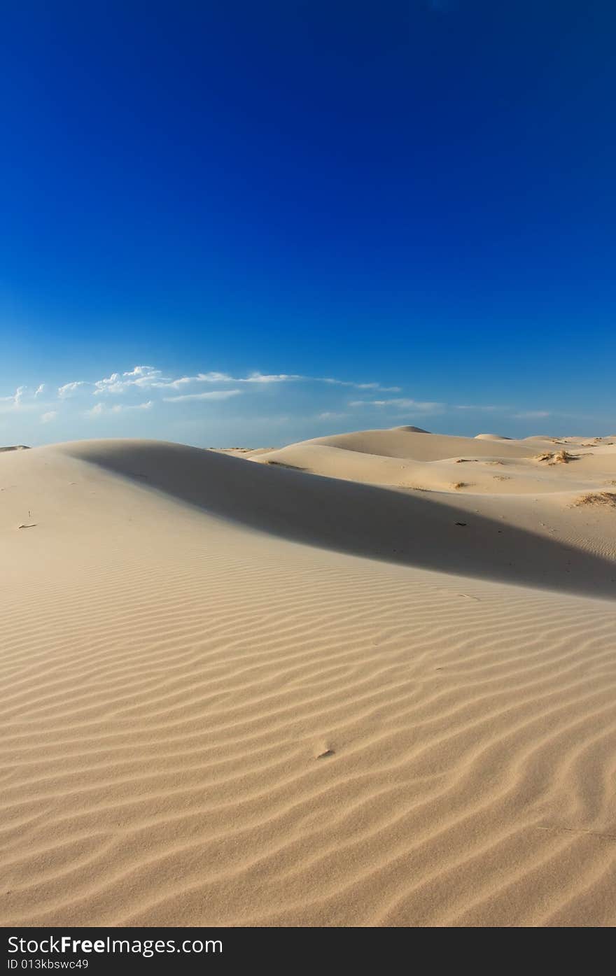 An image of windswept sand dunes on a blue sky. An image of windswept sand dunes on a blue sky