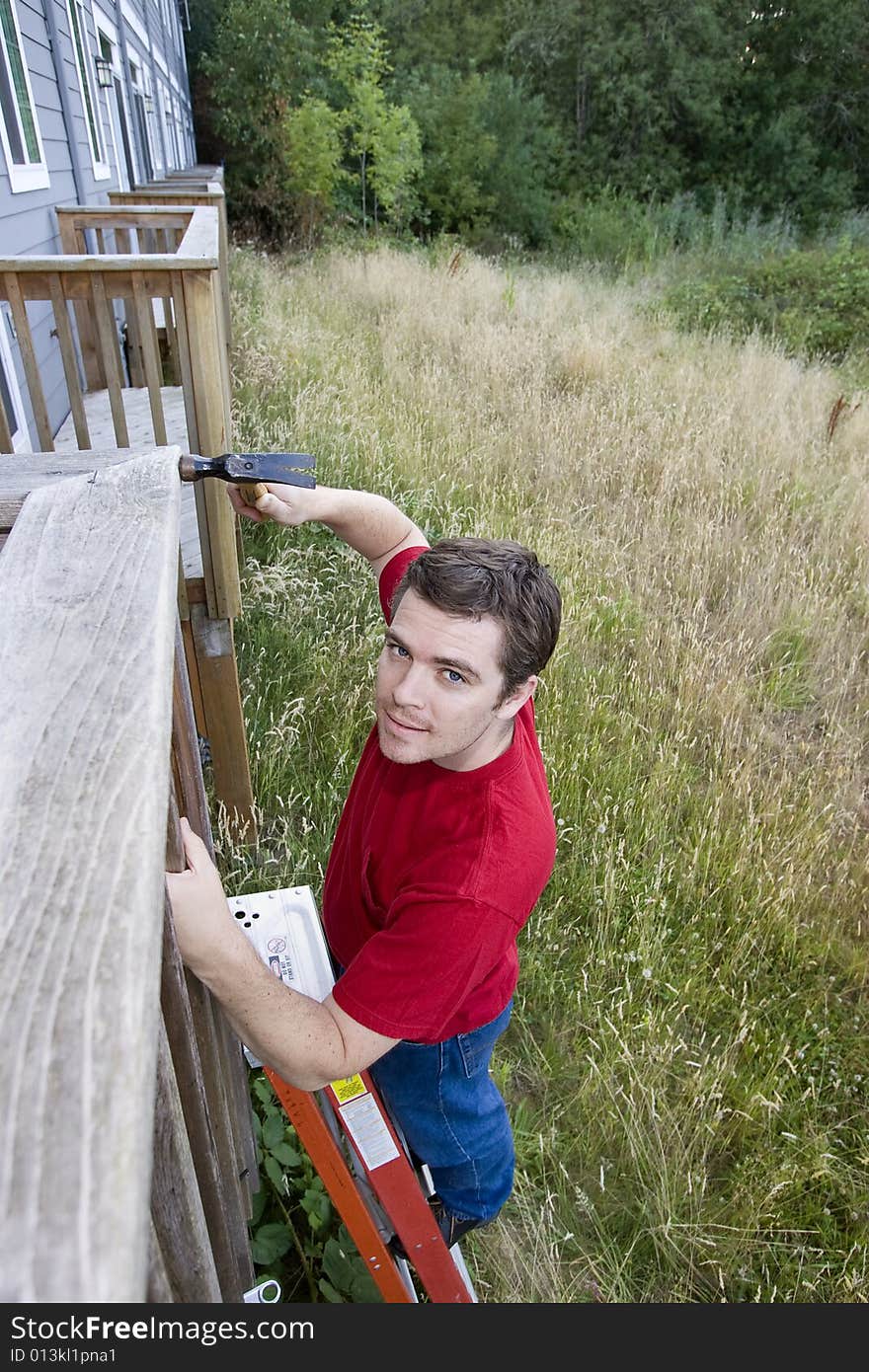 Man standing on a ladder hammering a porch. Vertically framed photo. Man standing on a ladder hammering a porch. Vertically framed photo.