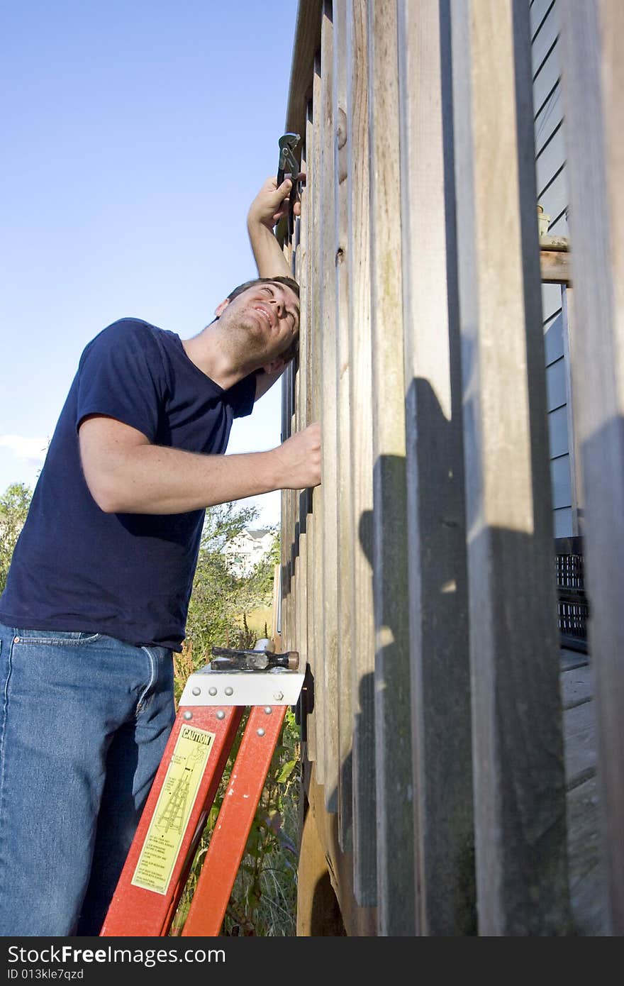 Man on a ladder repairing siding of a house with a wrench while looking up in the sky. Vertically framed photo. Man on a ladder repairing siding of a house with a wrench while looking up in the sky. Vertically framed photo.