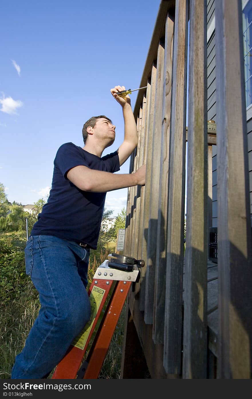 Man on a ladder repairing siding of a house with a screwdriver. Vertically framed photo. Man on a ladder repairing siding of a house with a screwdriver. Vertically framed photo.