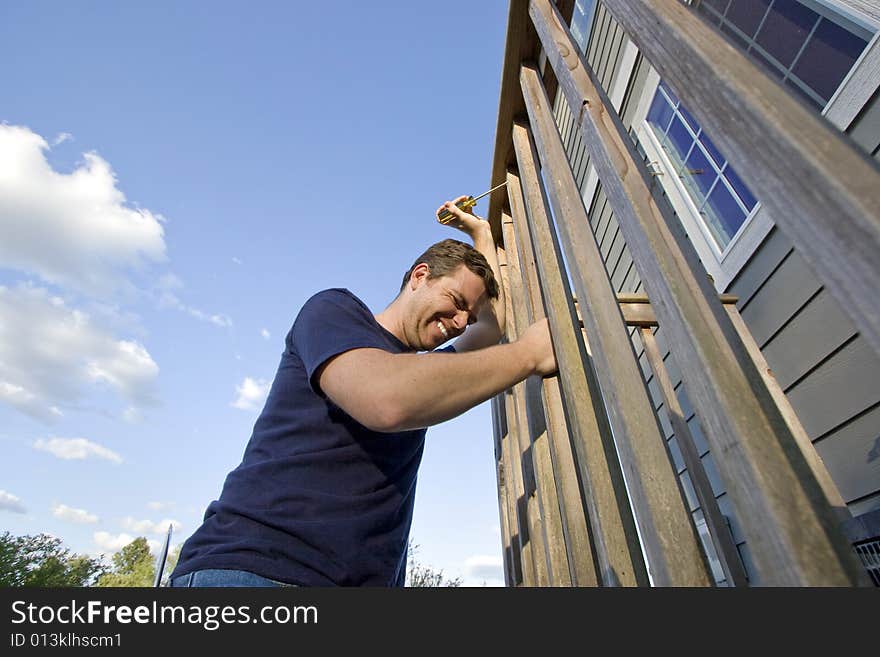 Frowning man fixing the siding on a house with a screwdriver. Horizontally framed photo. Frowning man fixing the siding on a house with a screwdriver. Horizontally framed photo.