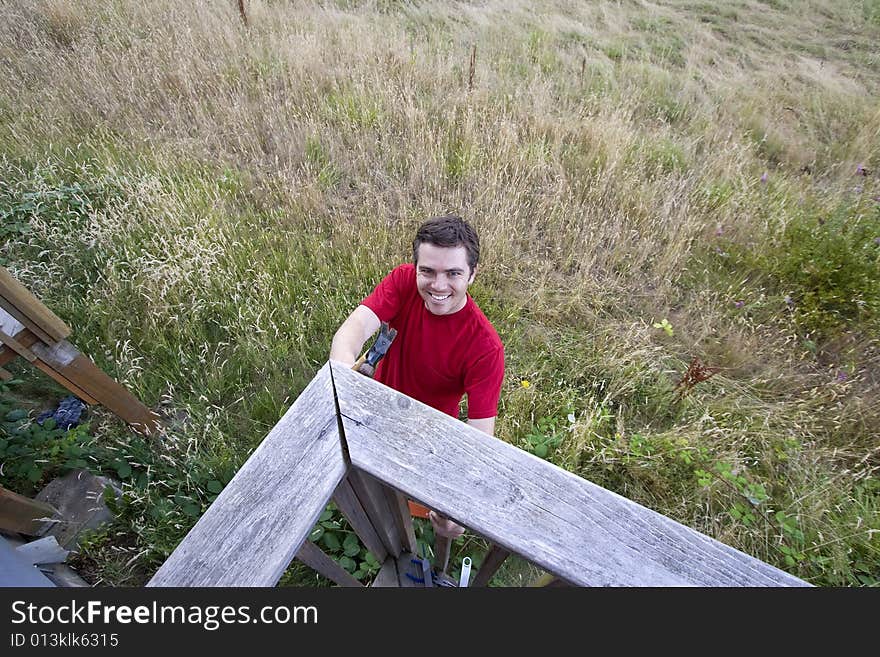 Aerial view of  a frowning man  on ladder hammering a porch. Horizontally framed photo. Aerial view of  a frowning man  on ladder hammering a porch. Horizontally framed photo.