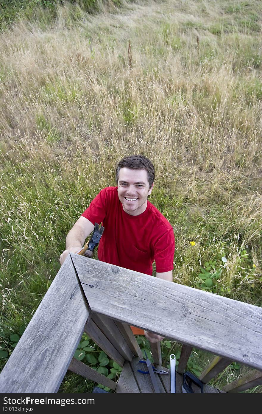 Aerial view of  a smiling man  on ladder hammering a porch. Vertically framed photo. Aerial view of  a smiling man  on ladder hammering a porch. Vertically framed photo.