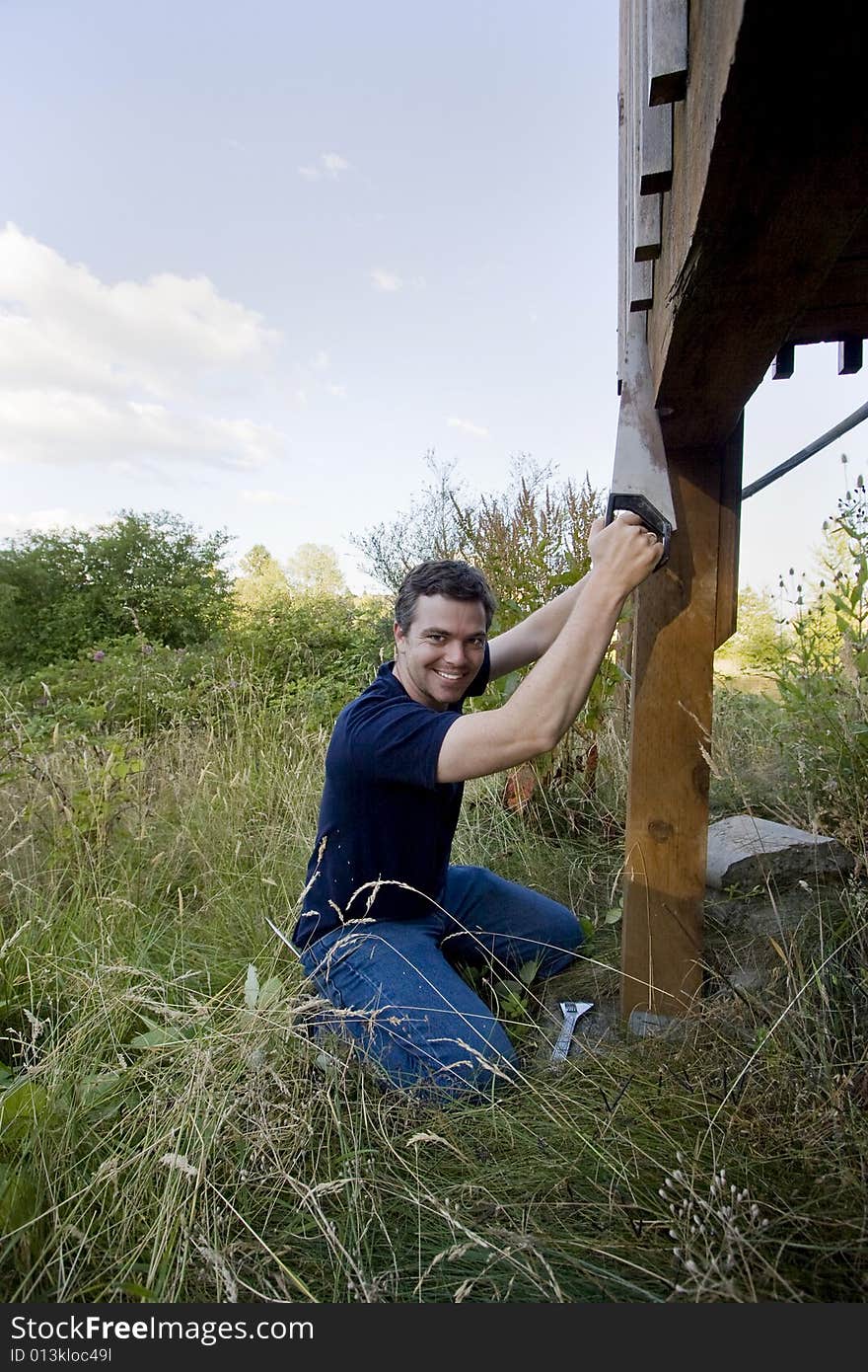 Man fixing a beam on a house with a saw. He looks happy and is smiling. Vertically framed photo. Man fixing a beam on a house with a saw. He looks happy and is smiling. Vertically framed photo.