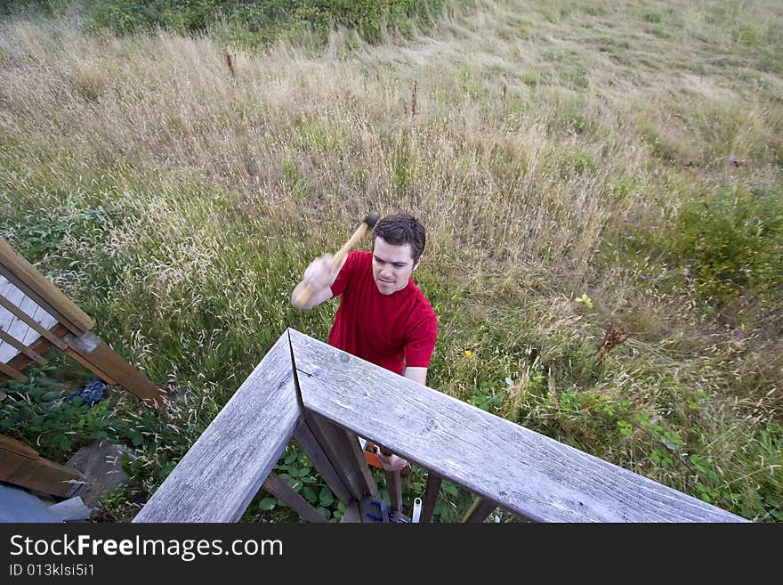 Aerial view of man on ladder hammering a porch. Horizontally framed photo. Aerial view of man on ladder hammering a porch. Horizontally framed photo.