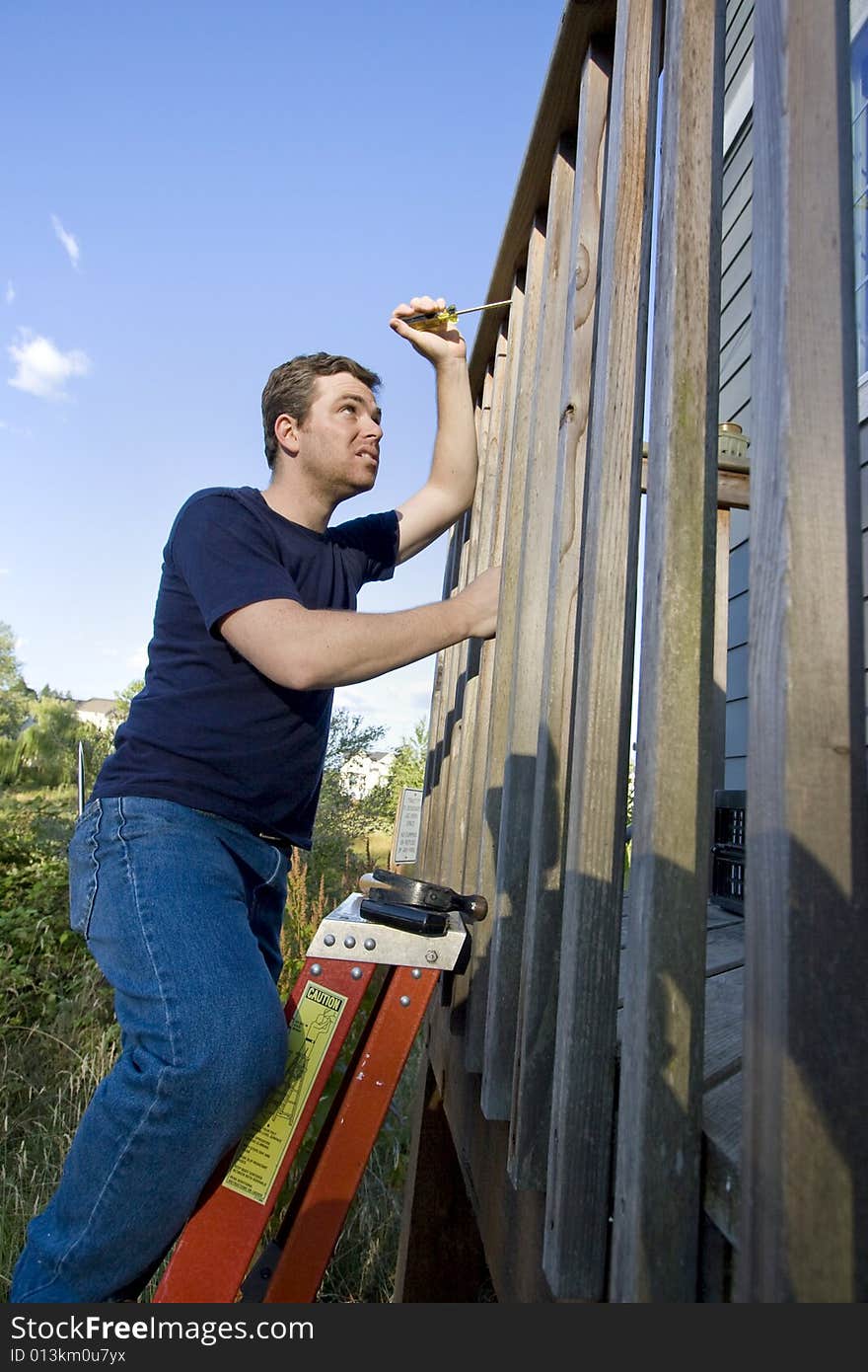 Man on ladder fixing the siding on a house with a screwdriver. Vertically framed photo. Man on ladder fixing the siding on a house with a screwdriver. Vertically framed photo.