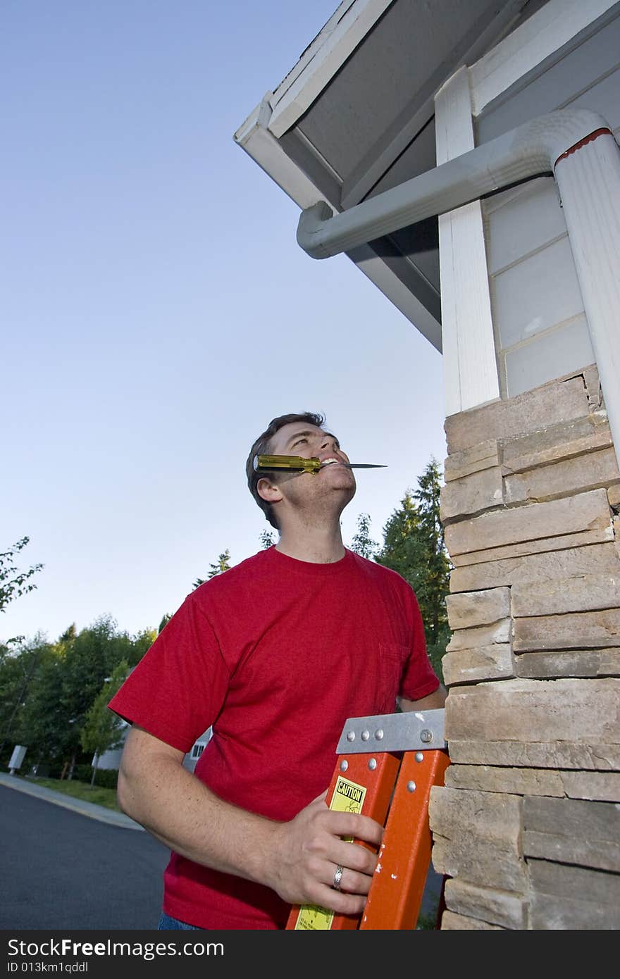 Man with a  screwdriver in his mouth standing on a ladder looking up at a house. Vertically framed photo. Man with a  screwdriver in his mouth standing on a ladder looking up at a house. Vertically framed photo.