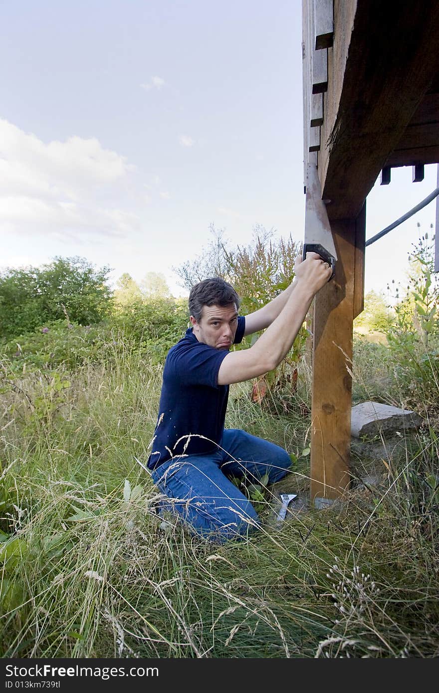 Man fixing a beam on a house with a saw. He looks unhappy . Vertically framed photo. Man fixing a beam on a house with a saw. He looks unhappy . Vertically framed photo.