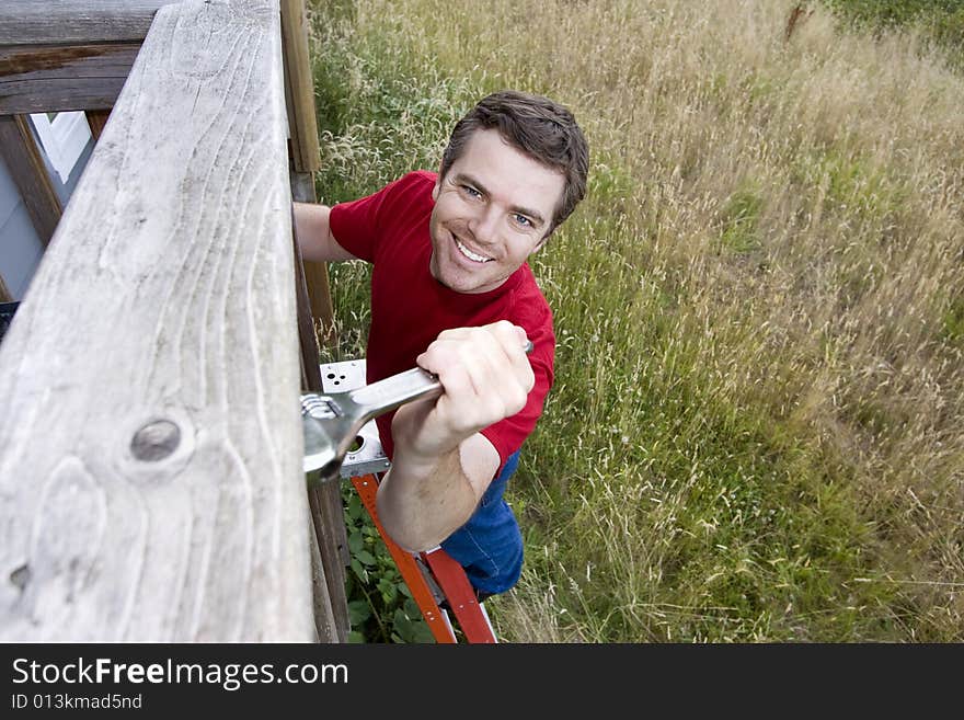 Happy man standing on a ladder fixing a porch with a wrench. Horizontally framed photo. Happy man standing on a ladder fixing a porch with a wrench. Horizontally framed photo.