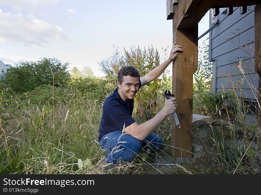 Smiling man fixing a beam on a house with a wrench. Horizontally framed photo. Smiling man fixing a beam on a house with a wrench. Horizontally framed photo.