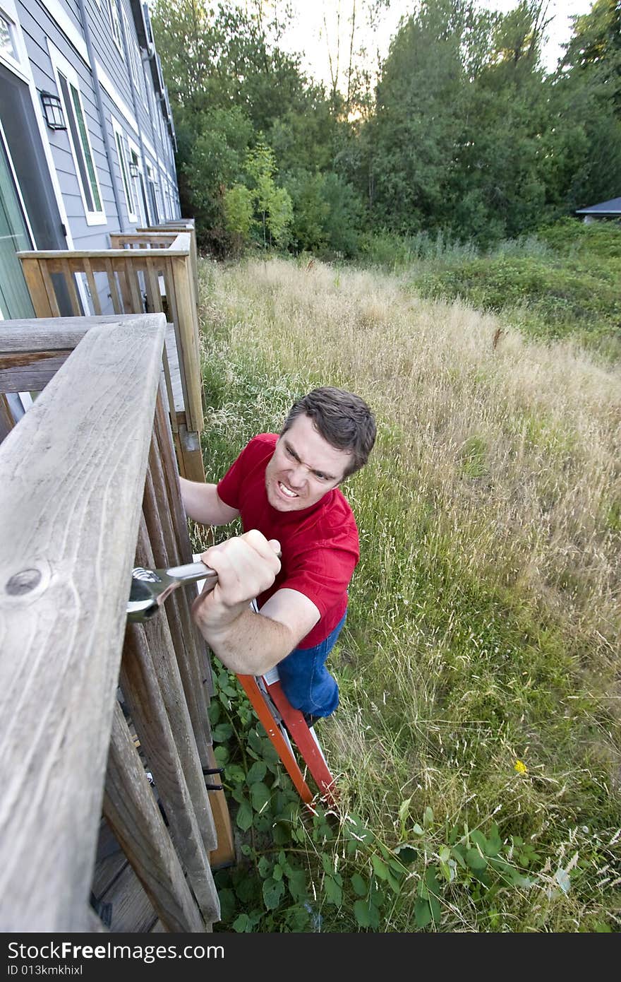 Man with a  grimace on his face standing on a ladder fixing a porch with a wrench. Vertically framed photo. Man with a  grimace on his face standing on a ladder fixing a porch with a wrench. Vertically framed photo.