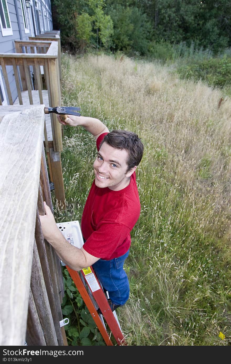 Man standing on a ladder hammering a porch. Vertically framed photo. Man standing on a ladder hammering a porch. Vertically framed photo.